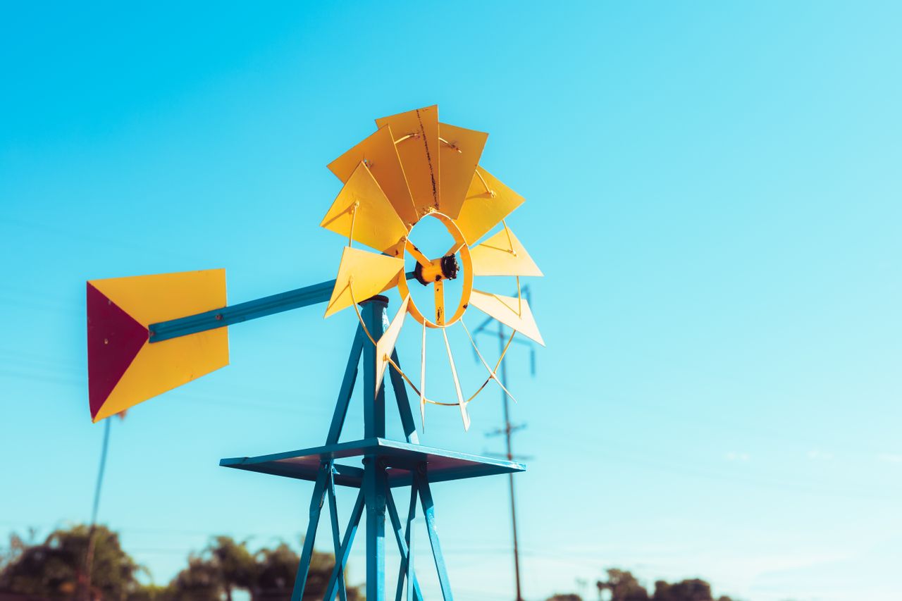 Close-up of a vibrant yellow windmill against a clear blue summer sky.
