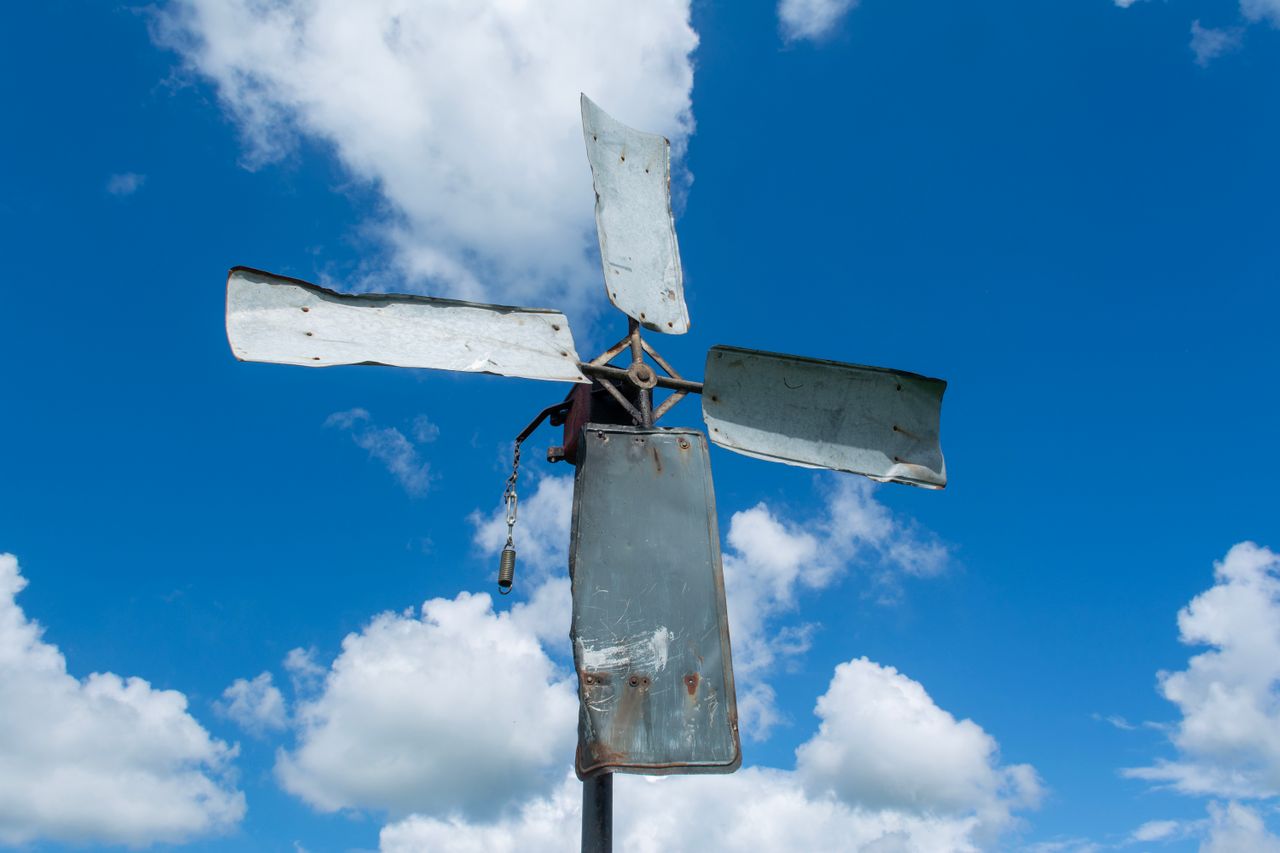 services-02 A rustic metal windmill stands tall under a vivid blue sky with scattered clouds.