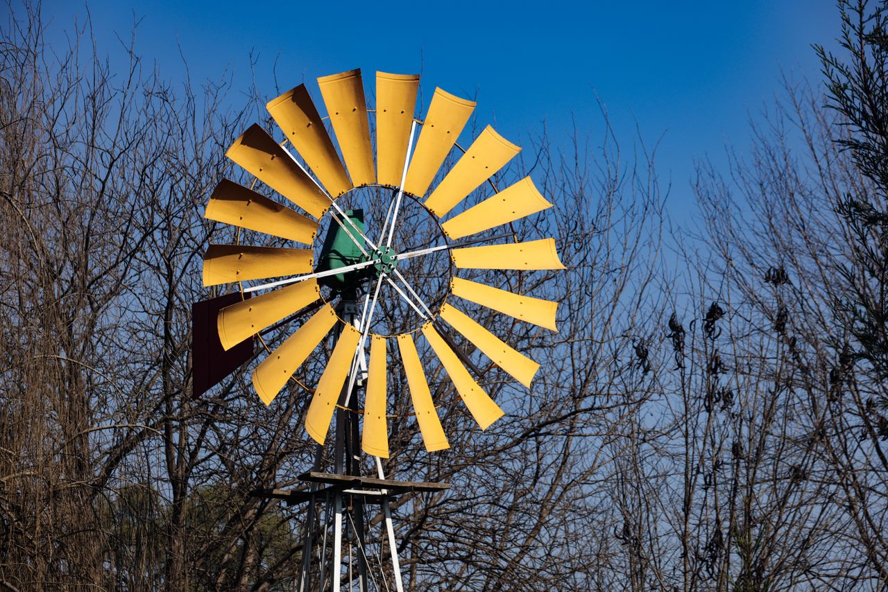 services-01 A yellow windmill stands tall against a clear blue sky with bare winter trees in background.